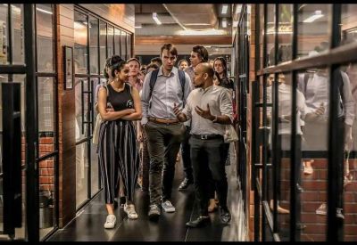Glass-walled corridor with people walking past private office suites
