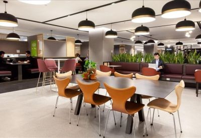 Modern breakout space featuring numerous pendant lights and stylish orange-backed chairs.