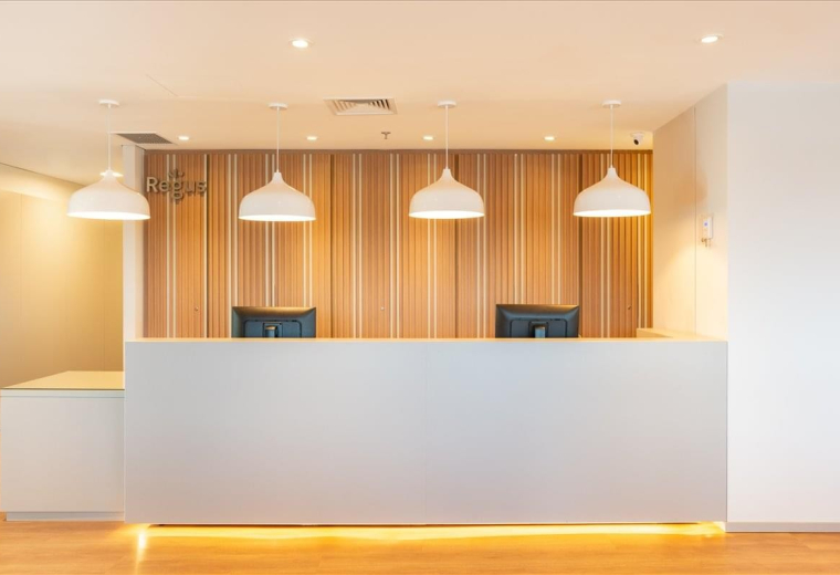 Professional reception area featuring a clean white desk, warm wood-paneled walls, and hanging pendant lights.