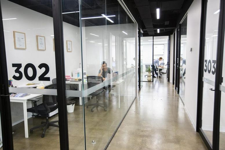 Bright glass-walled office suites along a modern corridor.