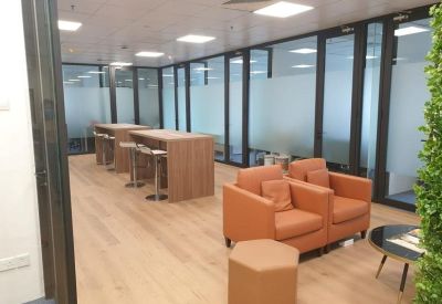 Modern breakout area with high tables, orange armchairs, and wood flooring.