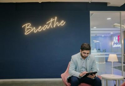 Reception area lounge with a navy blue feature wall displaying a neon Breathe sign.