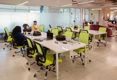 Open-plan workspace with multiple rows of white desks and bright lime green ergonomic chairs.