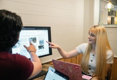 Two colleagues discussing digital content on a monitor in a modern office setting.