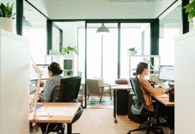 Bright open-plan office space with individual desks separated by glass partitions and shelving.