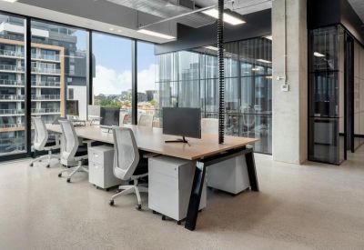 Open-plan office area with rows of desks and ergonomic white chairs by a window.