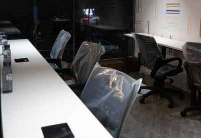Long white communal desk with ergonomic chairs and view of the street through dark windows.
