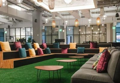 Casual communal lounge with tiered wooden seating, green turf flooring, and colorful throw pillows.