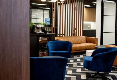 Stylishly furnished breakout area with navy velvet armchairs, tan leather sofa, and chevron patterned carpet.