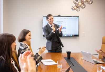 Professional business presentation taking place in a boardroom with attendees clapping.