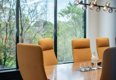 Executive boardroom with tan leather chairs and large windows overlooking lush greenery.