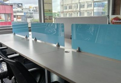Row of desks with blue partitions and black chairs by a window with city views.
