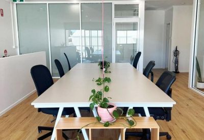 Open-plan coworking area with a large white table and wooden shelving unit.