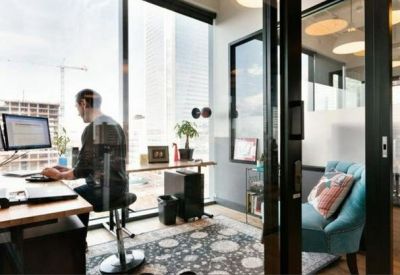 Private office space with glass walls, a patterned rug, and a person working at a computer desk.