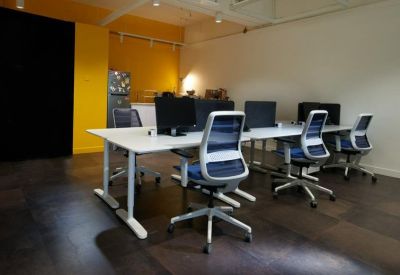 Bright open-plan workspace featuring white desks and ergonomic blue chairs against a yellow accent wall.