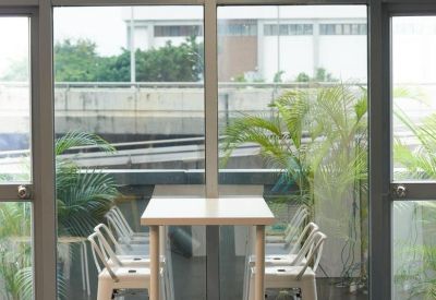 High bar-height communal table with white stools by a large window overlooking the city.