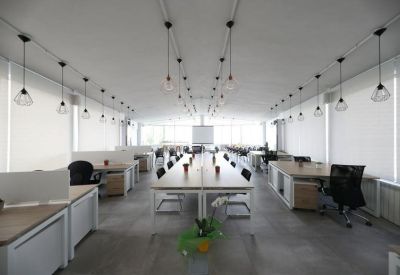 Bright open-plan office space with long rows of desks and industrial-style pendant lighting.
