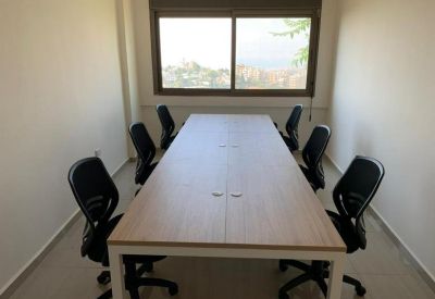 Meeting room with a long light-wood table and six black ergonomic chairs near a window.