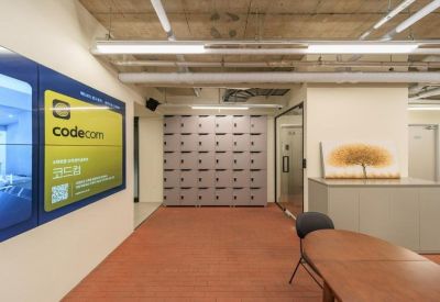 Reception area with a large digital display, grey storage lockers, and a wooden meeting table.