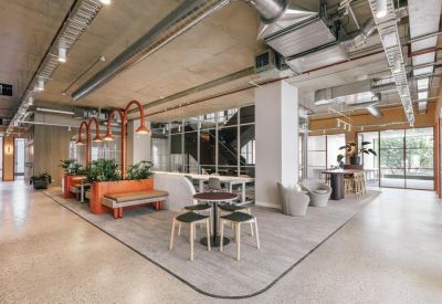 Spacious breakout area with curved lounge, plants, and industrial ceiling.