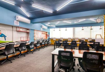 Spacious coworking area with blue walls, long rows of desks, and bright overhead lighting.