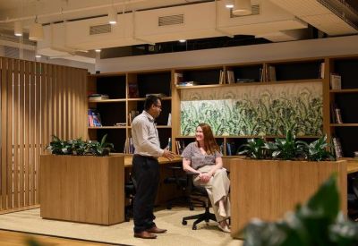 Two people talking in a modern office lounge area with wooden partitions and bookshelves.