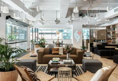 Contemporary office lobby with a brown leather sofa, potted palms, and high industrial ceilings.