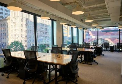 Bright open-plan office with wooden desks and large windows overlooking city buildings.