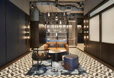Lounge area with a leather sofa and blue pouf on a patterned rug.