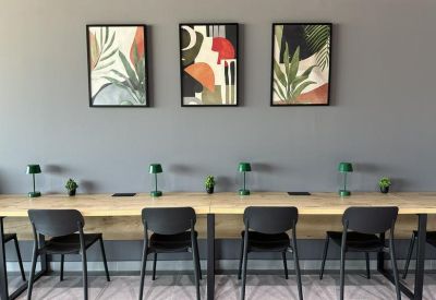 Long wooden shared workspace with black chairs and abstract botanical wall art.