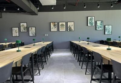 Spacious open-plan workspace with two long timber tables, desk lamps, and framed leaf prints.