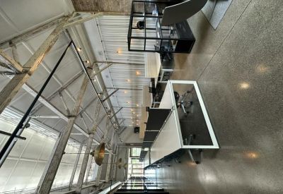 Long open-plan workspace with white desks and industrial ceiling beams.