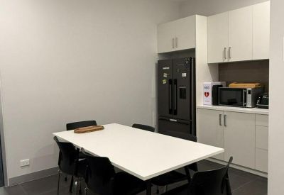 Modern communal kitchen and dining area with white cabinetry and dark tile flooring.