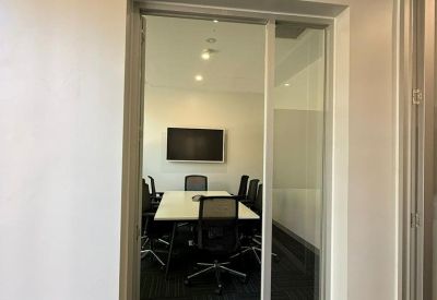 Glass-walled entrance looking into a bright conference room with a large screen.