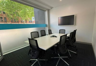 Professional meeting room with a white table, wall-mounted screen, and frosted window.