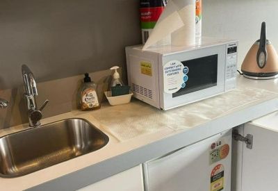 Modern communal kitchen area with a white microwave, sink, and mini fridge.