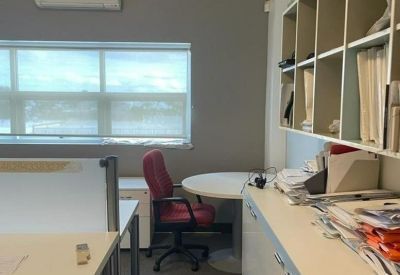 Bright office workspace with multiple desks, red chairs, and large windows.