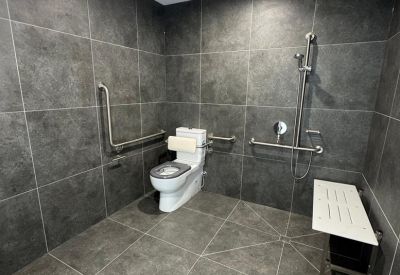 Modern accessible bathroom with dark grey stone tiling and stainless steel safety rails.