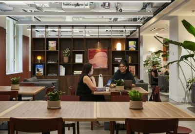 Communal dining and collaboration area with wooden tables, potted plants, and shelving.