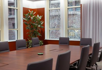 Sunlit boardroom with a large wooden table and views through classic arched windows.