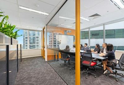 Glass-walled boardroom featuring a long black table and views of surrounding buildings.