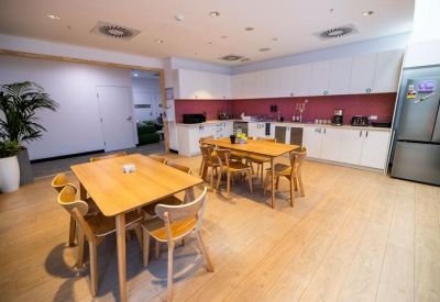 Spacious dining area with two large wooden tables and modern chairs near a kitchen.