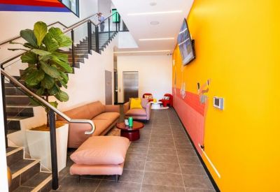 Inviting breakout lounge with a pink sofa, matching ottoman, and a bright yellow feature wall.