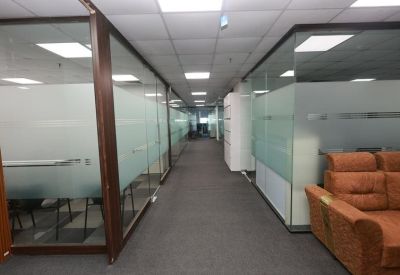Modern office corridor featuring glass-walled suites and a brown plush sofa.