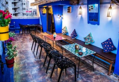 Open-air patio with blue walls, bistro tables, and hanging lanterns.