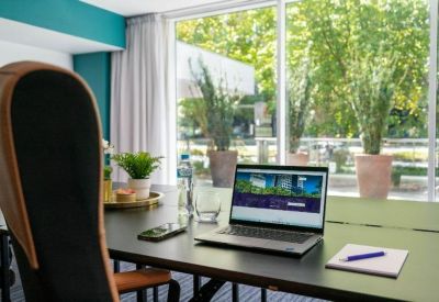 Close-up of a workspace desk with a laptop and view of green trees through the window.