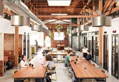 Large open-plan workspace featuring long wooden communal tables and exposed timber ceiling beams.