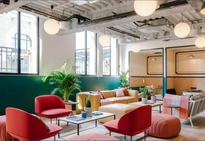Spacious breakout area with red armchairs, a yellow sofa, and high industrial ceilings with hanging lights.