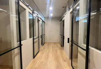 Corridor featuring glass-walled private office suites with black sliding barn doors.