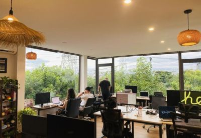 Modern open office layout with large windows, indoor plants, and straw lampshades.